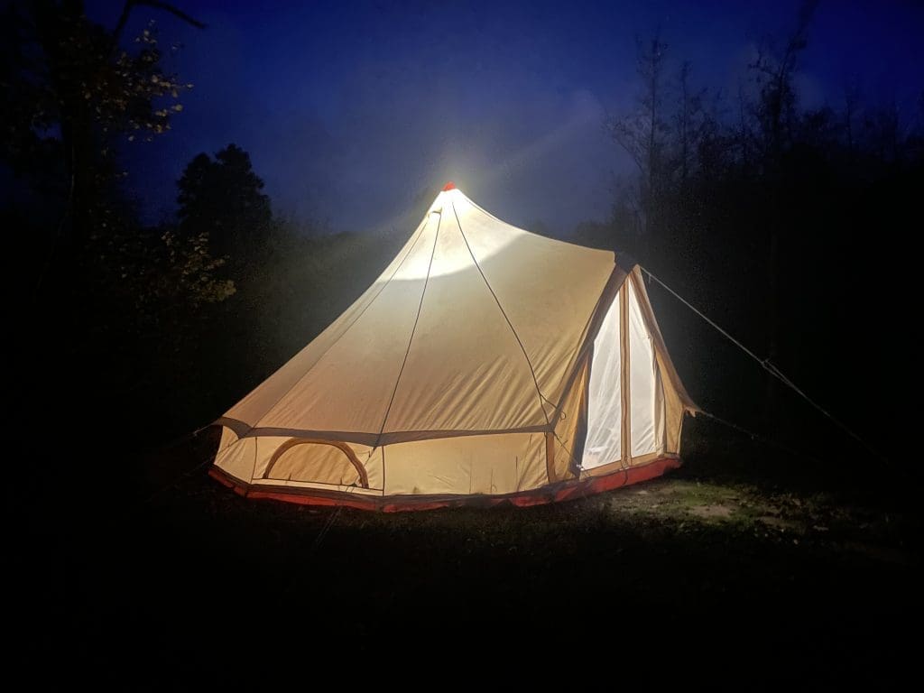a tent in the forest at night with a light on