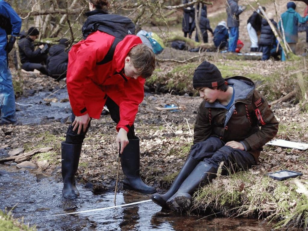 school group in a steam bed doing field study work in the stream