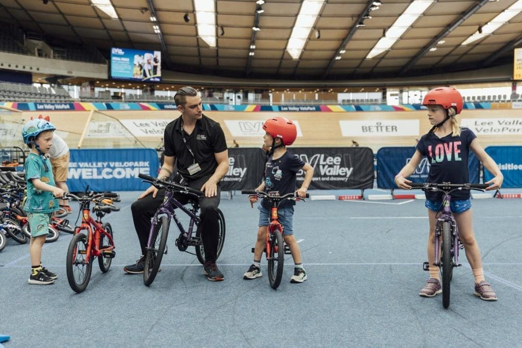 school pupils in an indoor cycle track on BMX bikes listing to an adult instructor