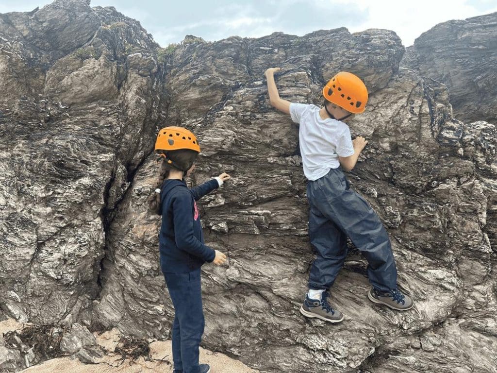 two primary school children with hard hats on climbing up a rock