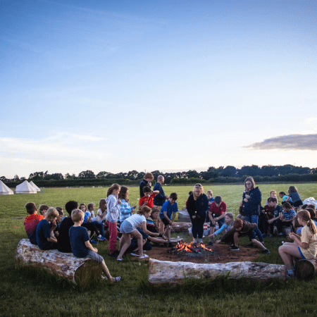 school group all sat around a fire pit in a field