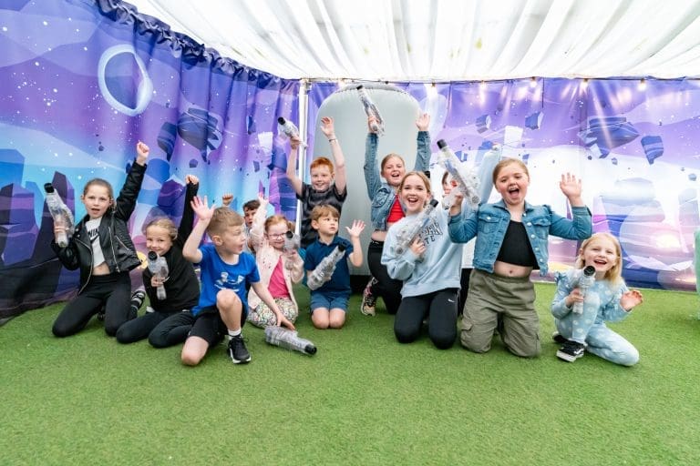 school pupils in an indoor tent smiling and waving
