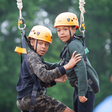 two primary school children on high ropes with hard hats and safety equipment on