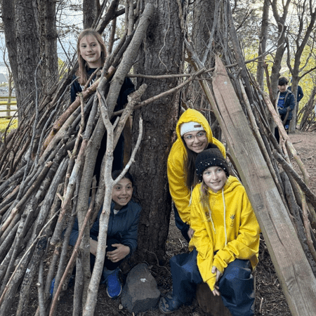 school group in a stick den they have built