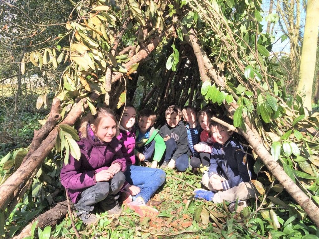 primary school students in forest made den of branches and leaves