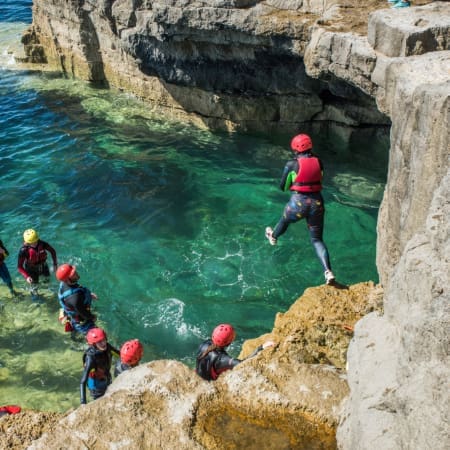 school students jumping into the sea of rocks with safety waterproofs on and hard hats