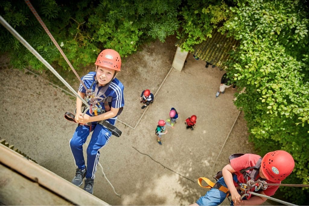 PGL Green Park School Trips 9 pupils with safety gear and hard hats on a abseiling tower abseiling down