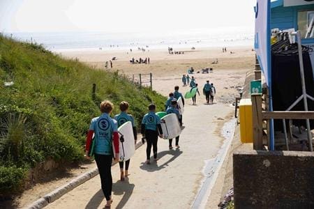 school pupils in wets suits walking down to the beach with surf boards