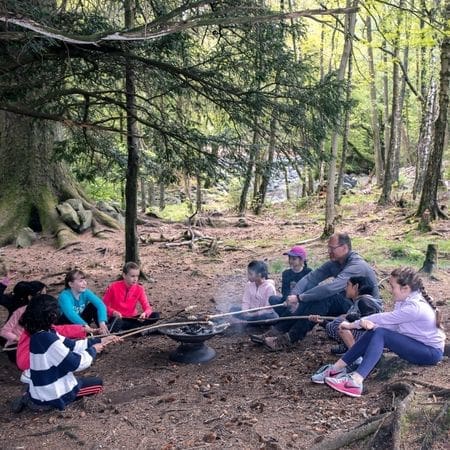 school group along with instructor around an open fire heating marshmellows